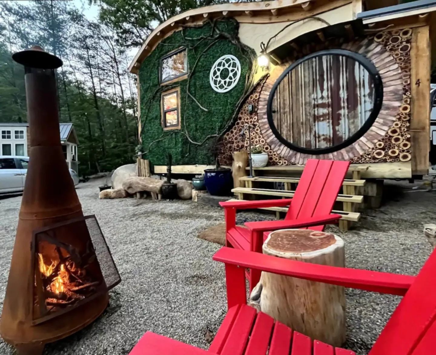 Tiny house with moss on the outside and an outdoor sitting area with a fire pit and red Adirondack chairs