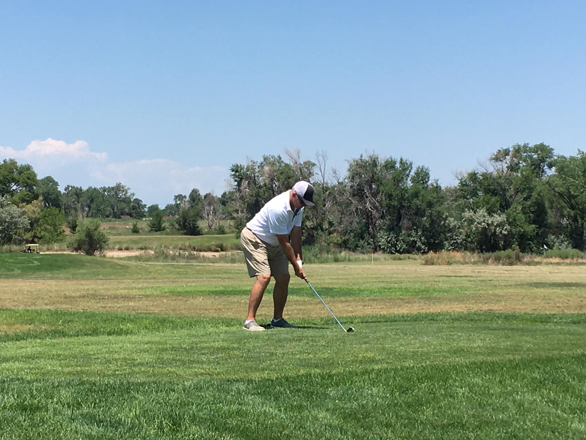 Person in short sleeve white shirt and white hat about to swing at a golf ball on the Cottonwood Links Golf Course