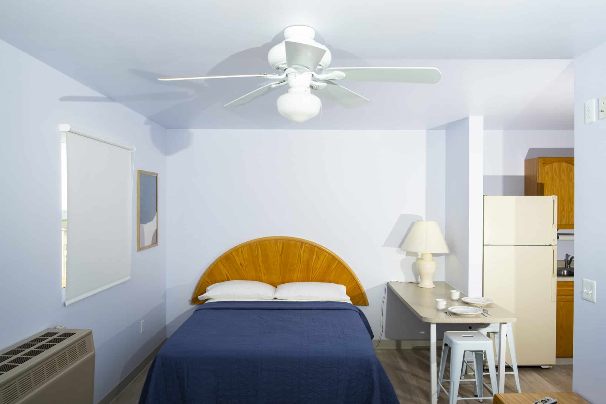 Plain hotel room with blue walls, wooden headboard on a queen bed with navy sheets