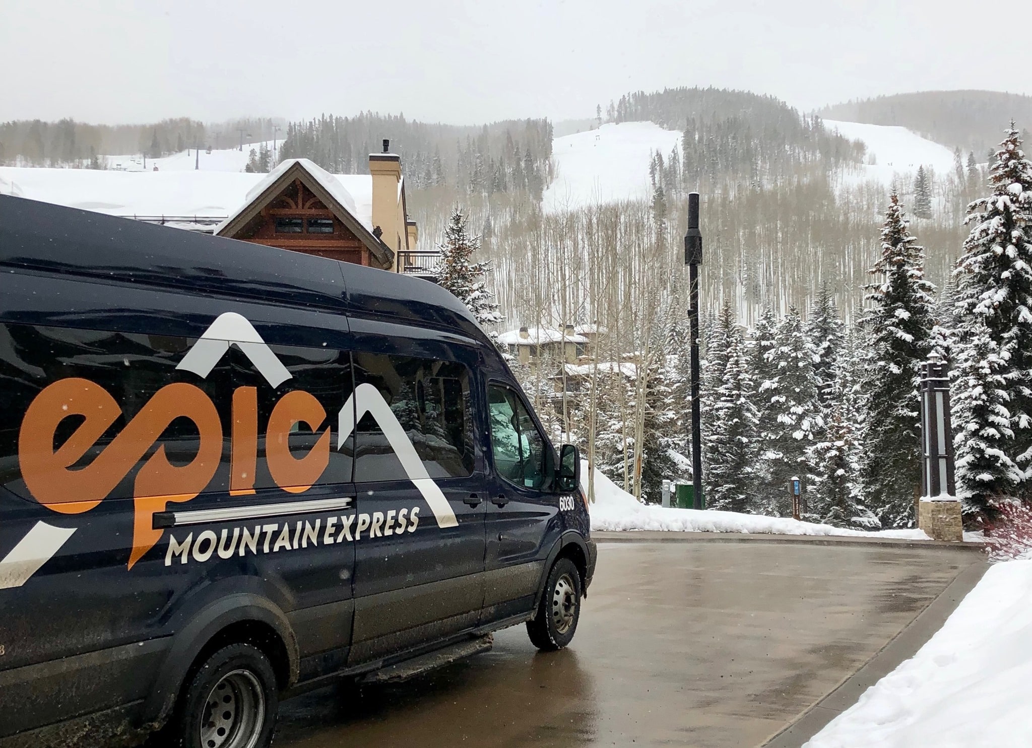 Black van with Epic Mountain Express written in yellow in a snowy parking lot