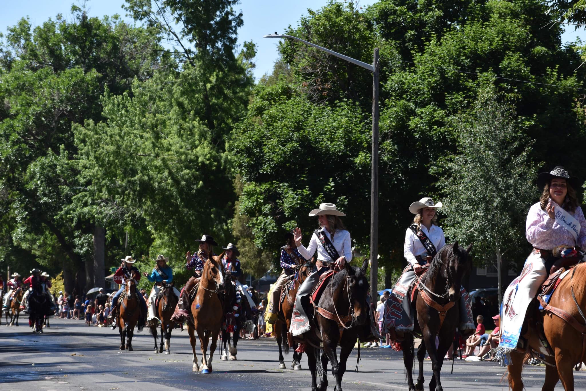 Parade menyusuri jalan dengan beberapa kuda dan cowgirl melambai