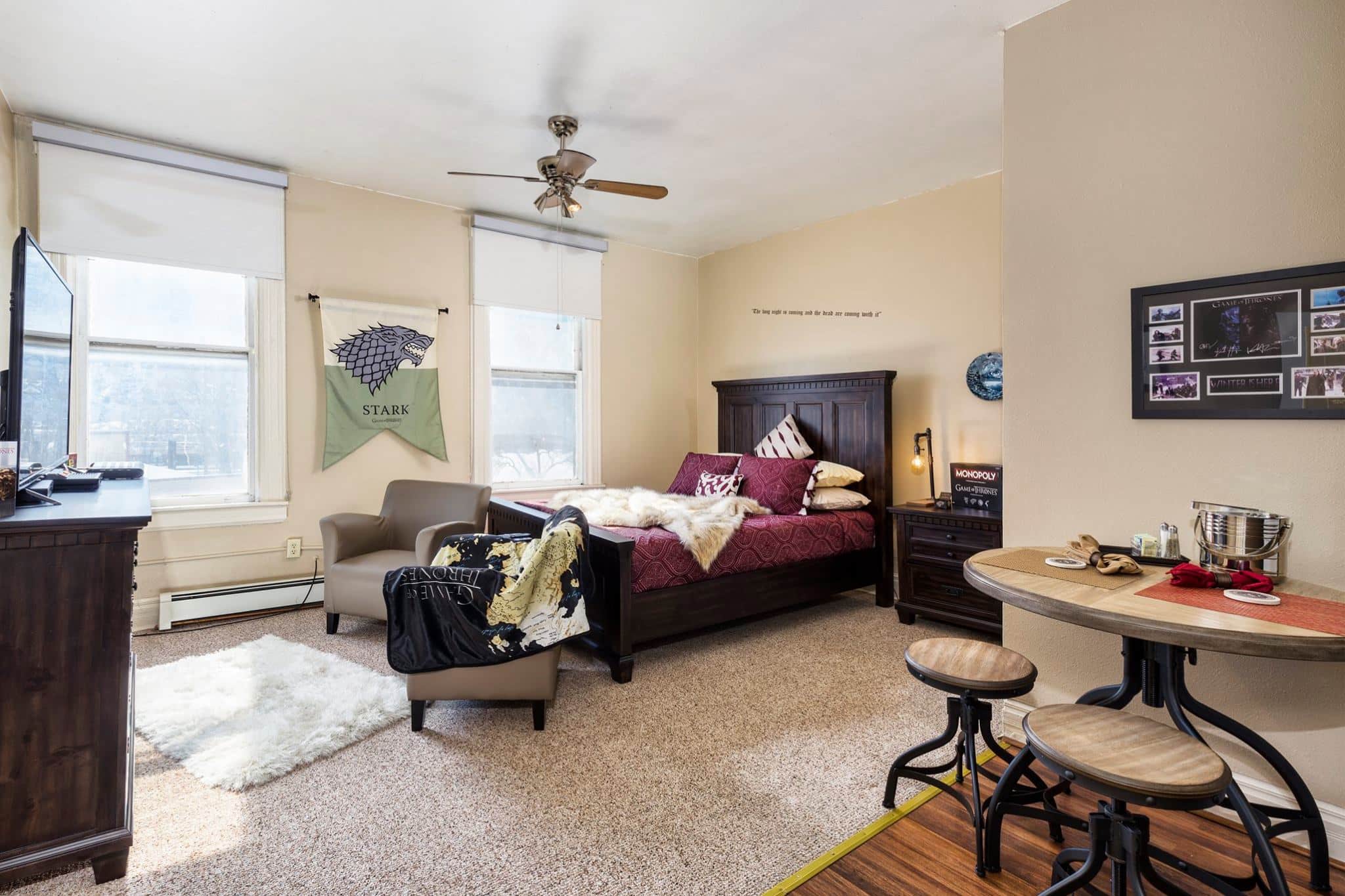 Spacious boutique hotel room with queen bed, burgundy linens, a large black headboard, and two sitting chairs at the foot of the bed. 