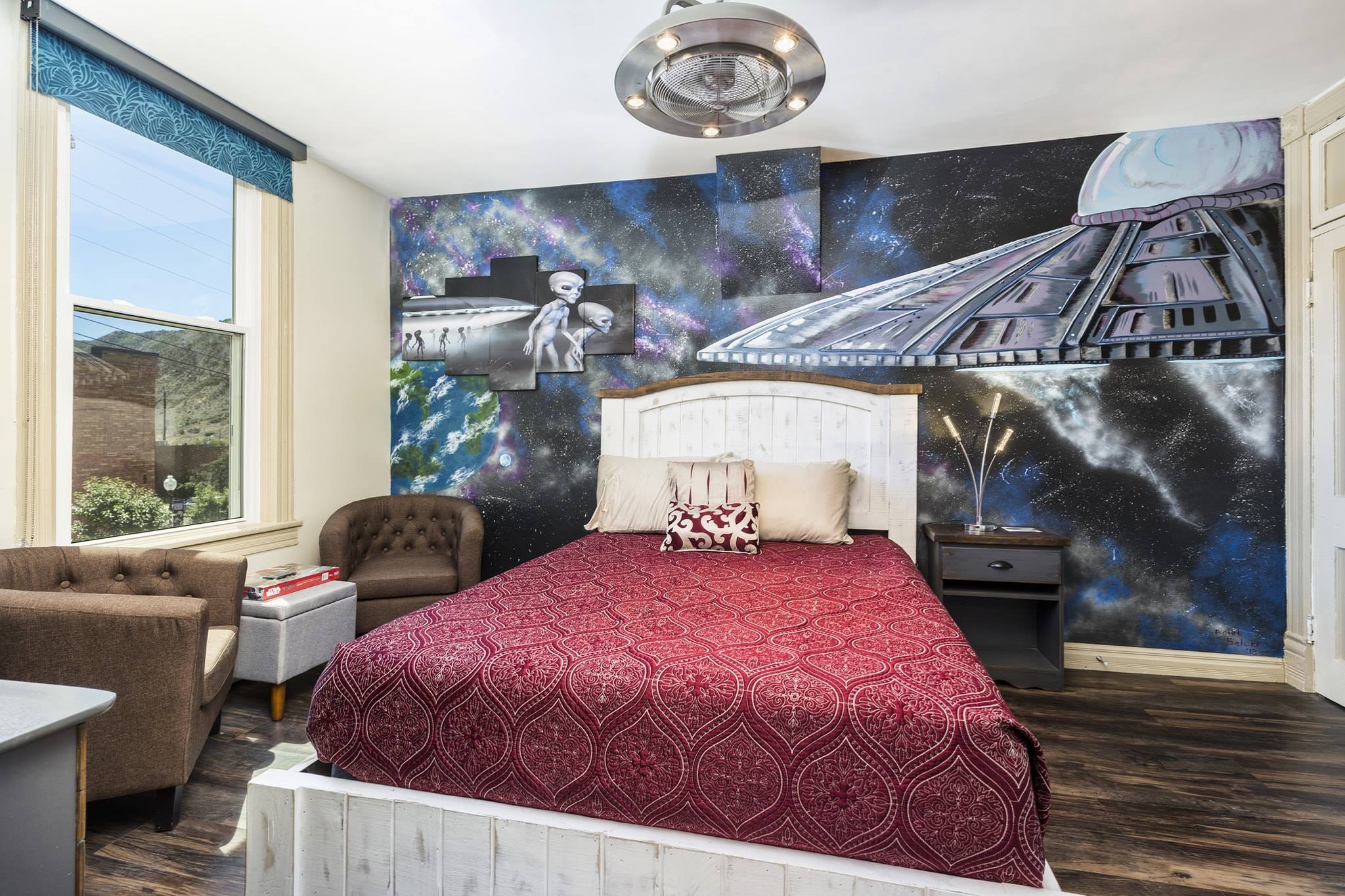 Alien themed boutique hotel room at the Ore House Inn. Wall painted with an outer space mural, white wooden bed frame with red bedding