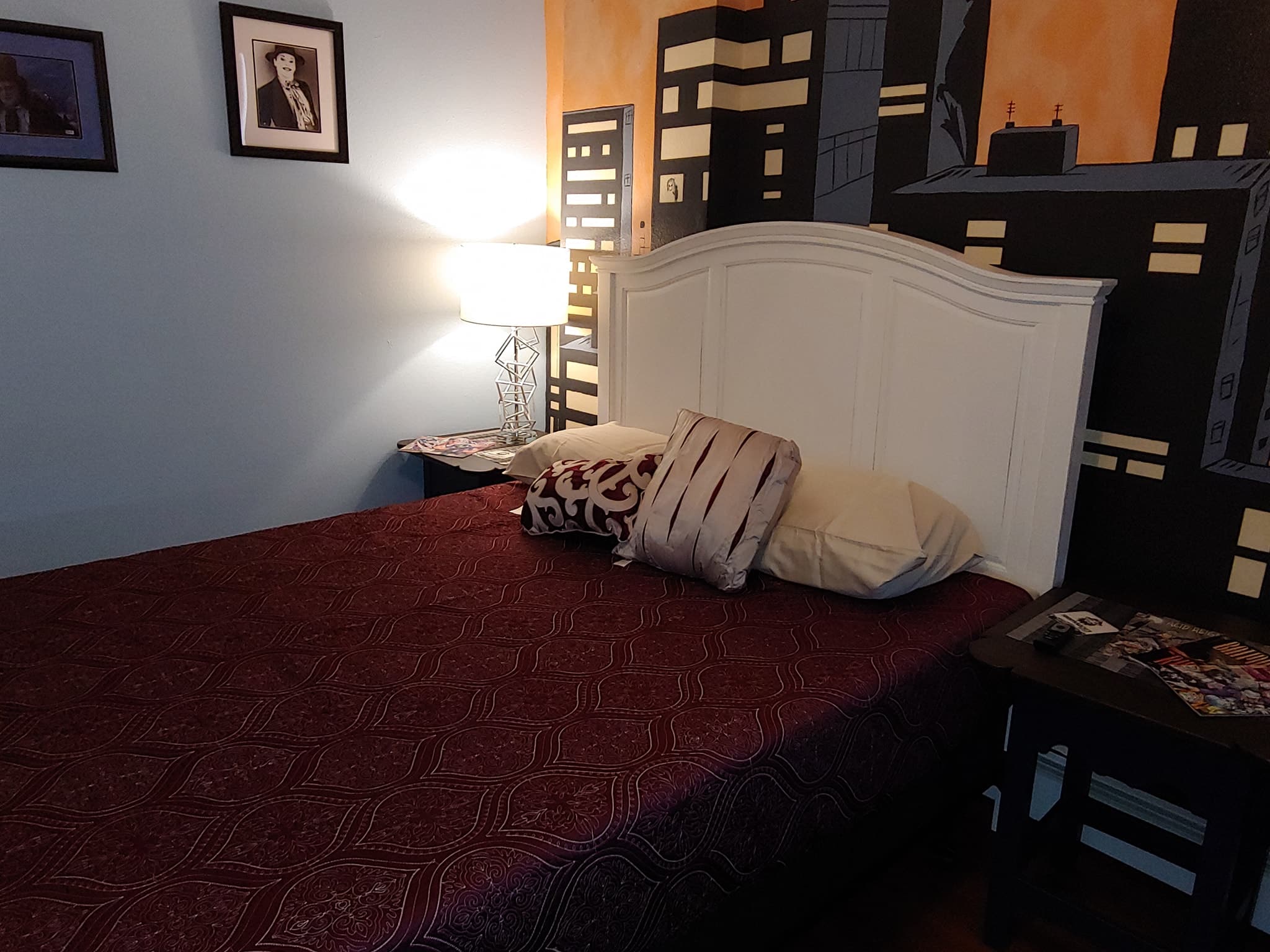 Hotel bedroom with queen bed in front of yellow and black city skyline mural at Ore House Inn