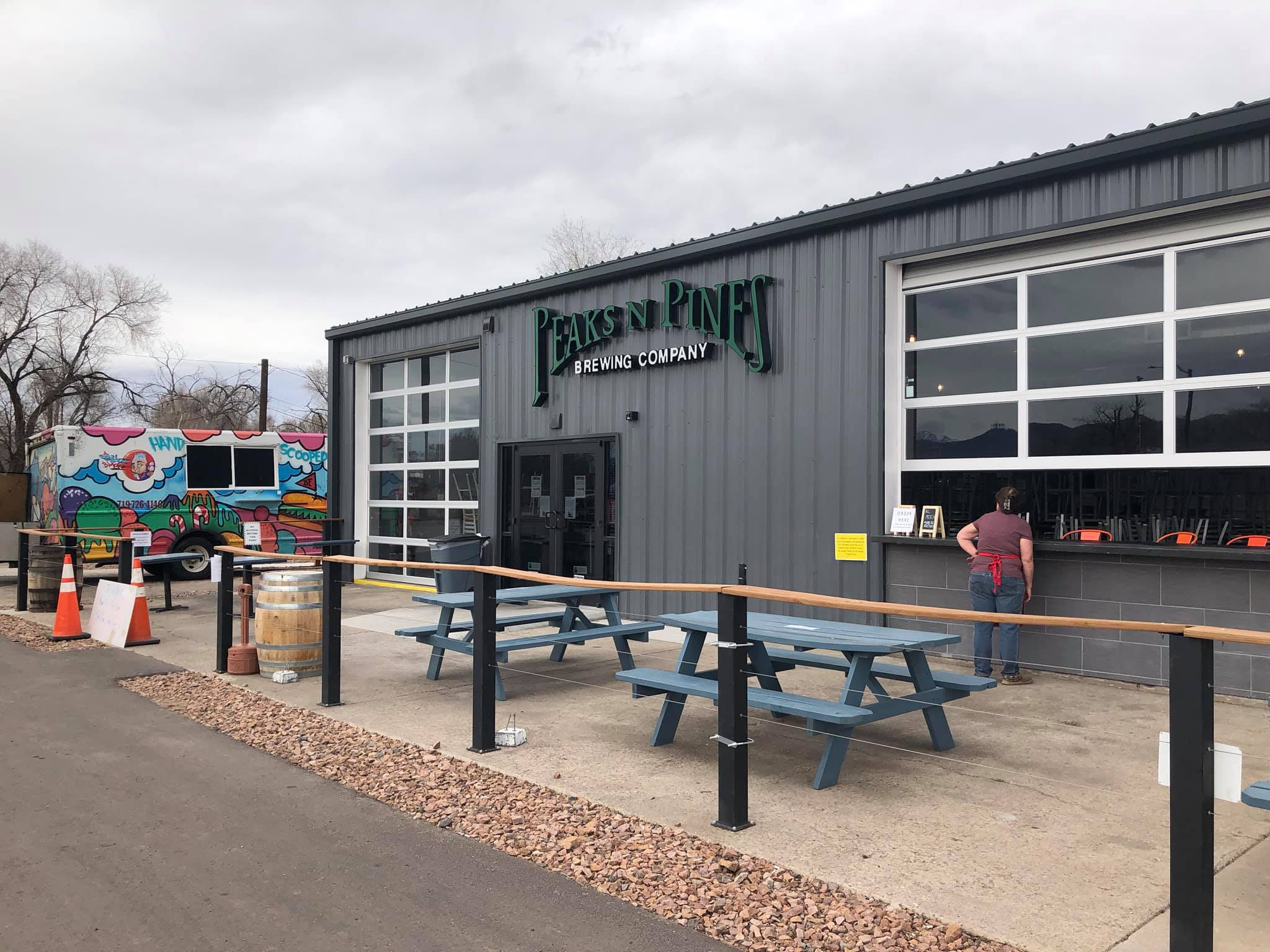 Front of a grey brewery building with picnic tables