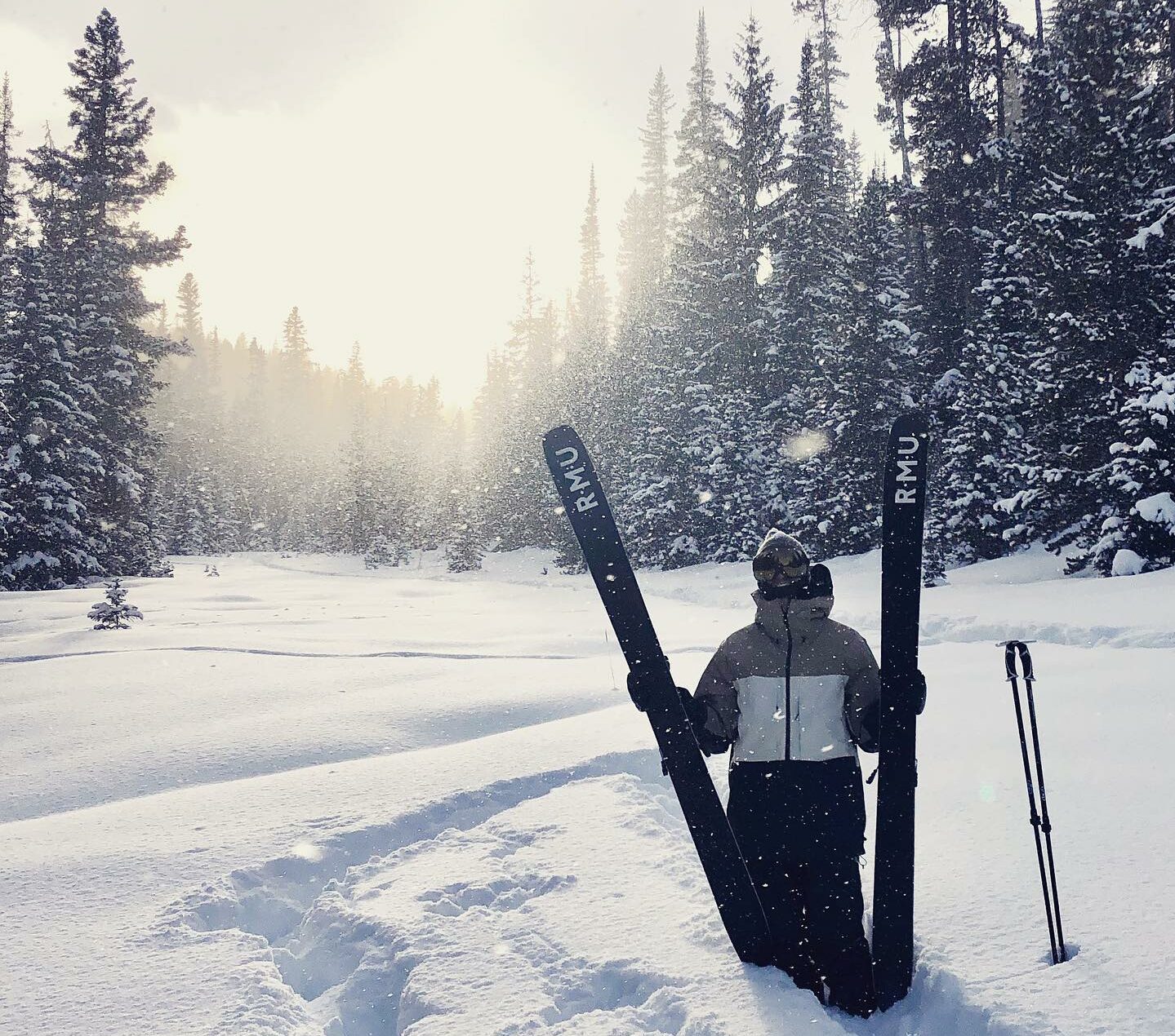 Pemain ski berjaket hitam berdiri di salju tebal di Breckenridge memegang dua ski hitam Rocky Mountain Underground