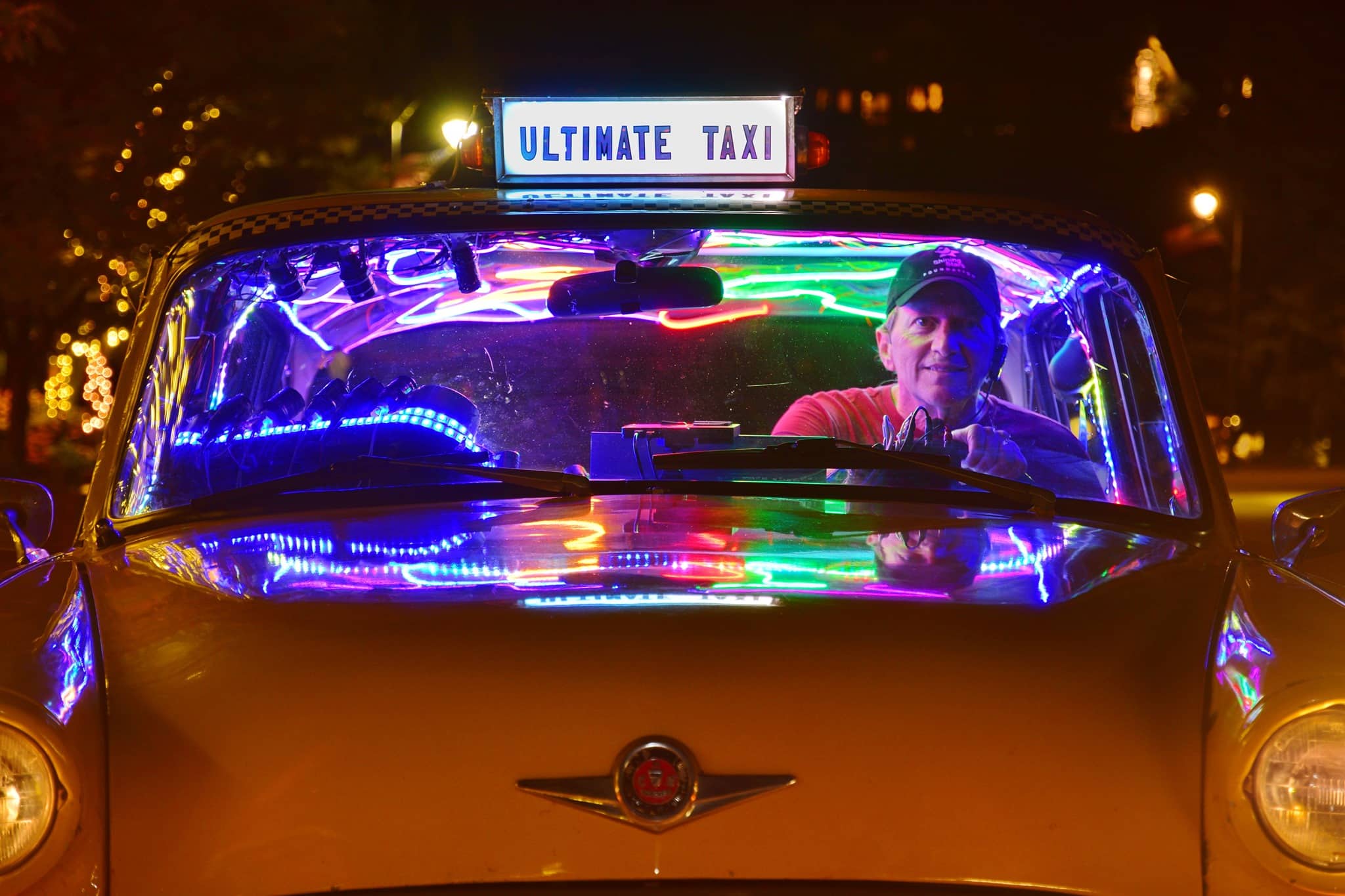 Yellow cab with neon lights inside and a happy driver