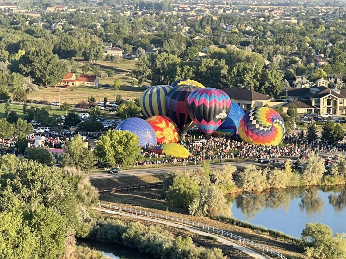 Numerous balloons blowing up to get ready for liftoff in a field next to a lake