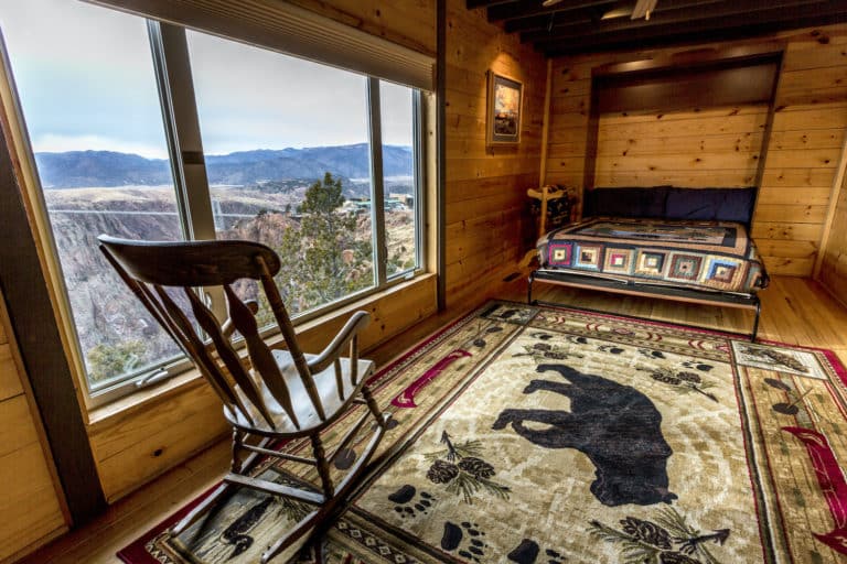 Room in the Bighorn Mountaintop Lodge at the Royal Gorge overlooking the gorge. There is a wooden rocking chair, large bear print rug, and a bed