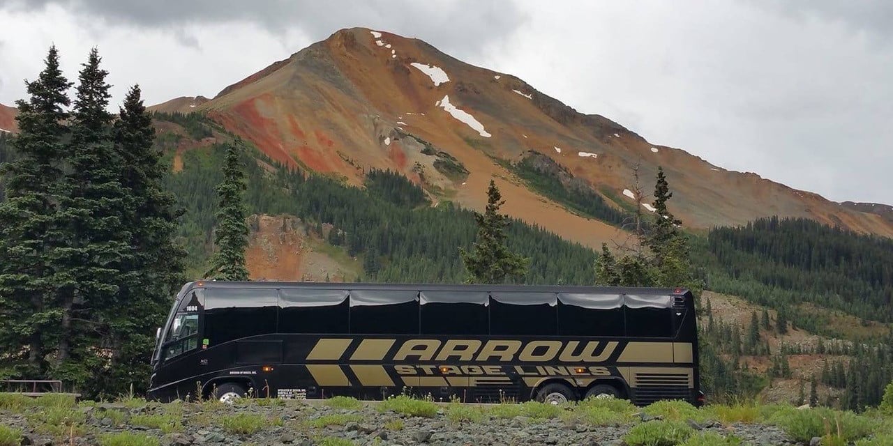 Black Arrow Stage Lines coach bus parked in front of a mountain with fall colors