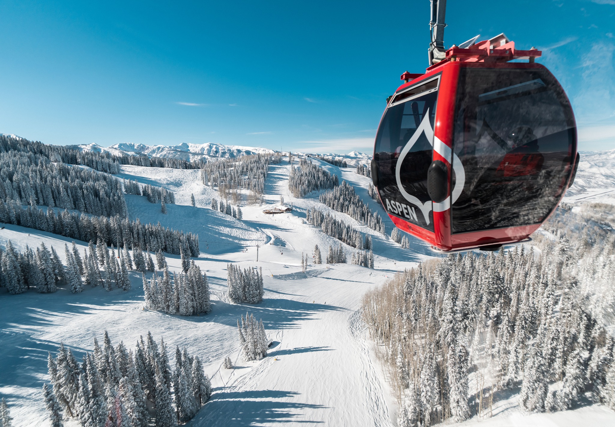 Bright red Aspen Snowmass enclosed gondola car in front of snowy mountain runs and clear blue skies