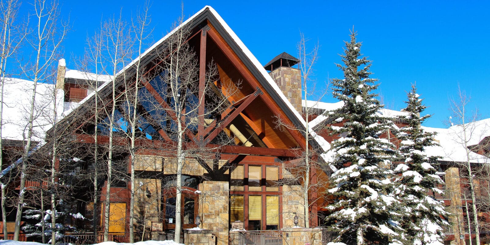 Front entrance to Bear Creek Lodge, a wooden A-frame building with several snow covered trees lining the entryway