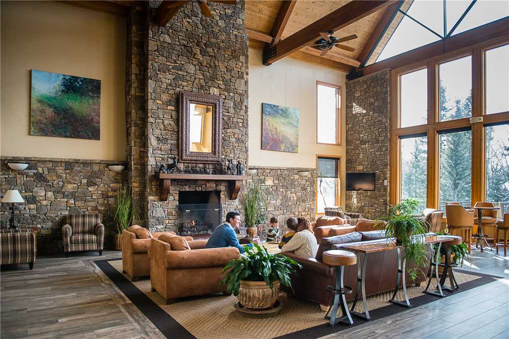 Lobby at Bear Creek Lodge with a huge stone fireplace, several plush sitting chairs, and vaulted ceilings with floor-to-ceiling windows letting in natural light. 