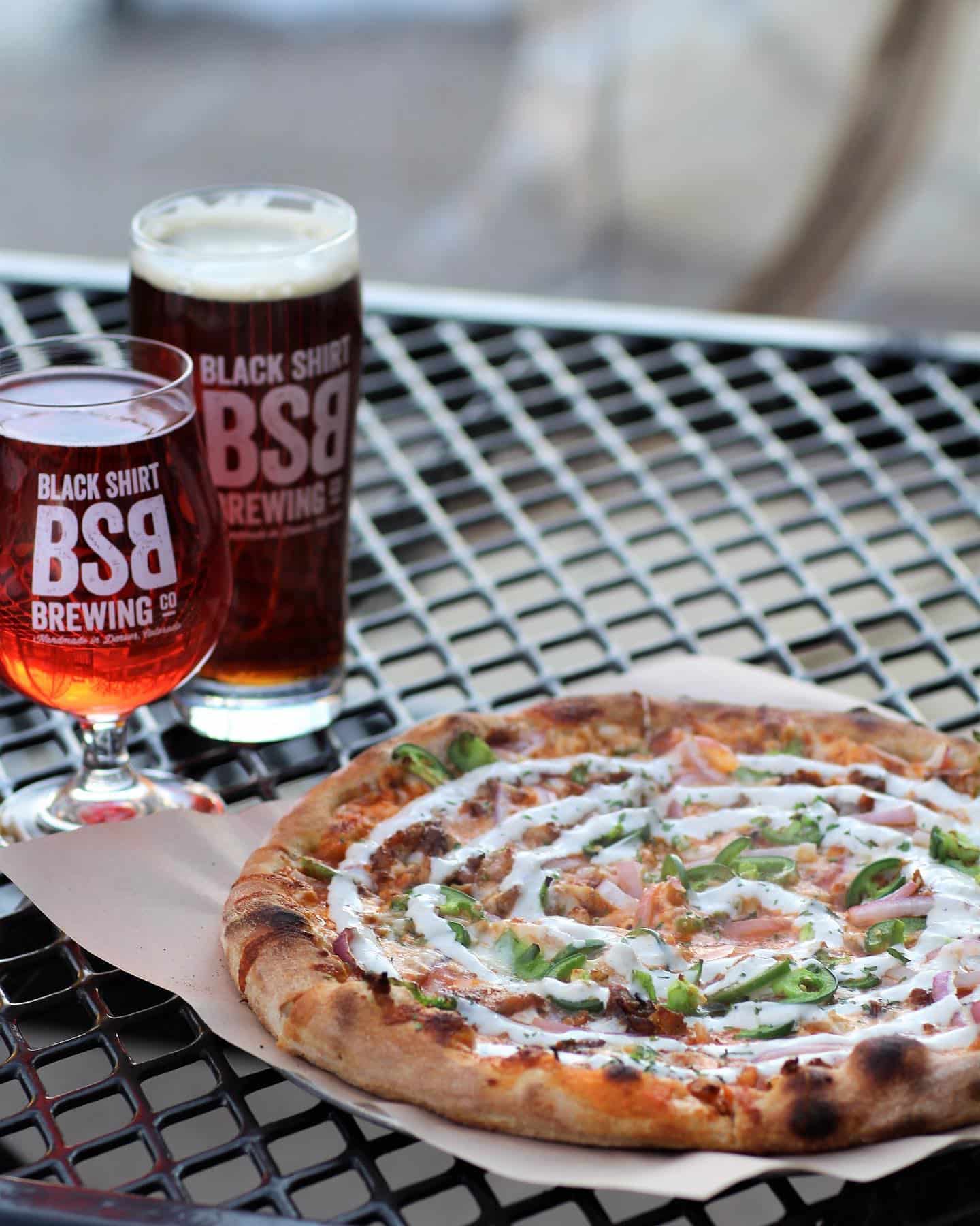 Outdoor table at Black Shirt Brewing Co. in Denver with 2 glasses of dark beer and a pizza