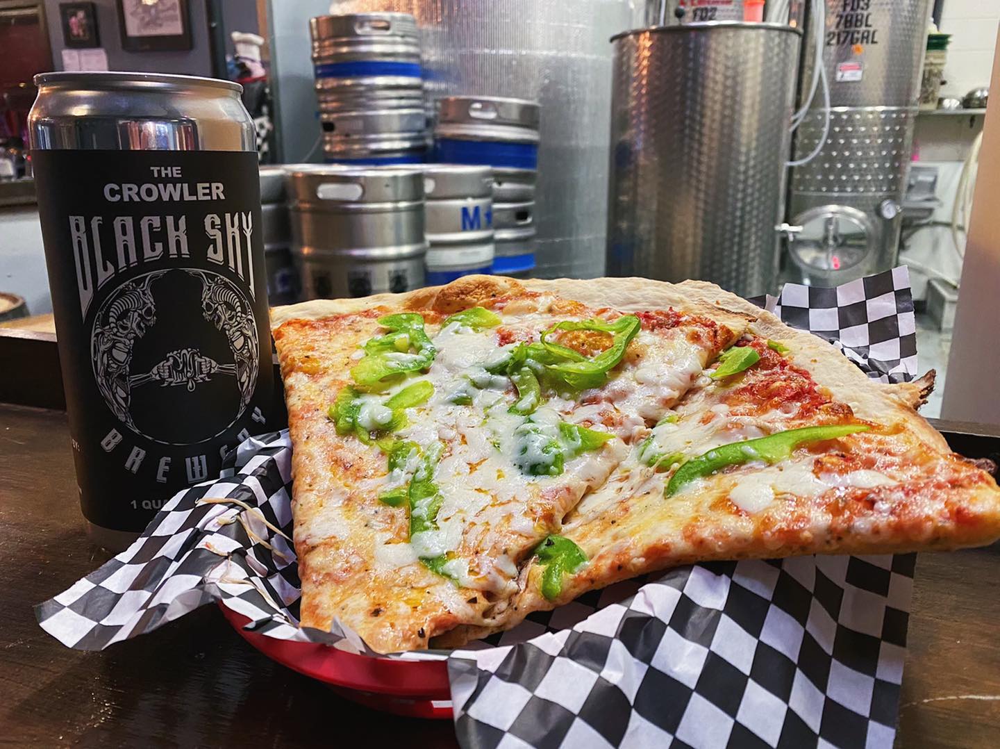 Two pieces of pizza in a plastic tray next to a can of Black Sky Brewery beer