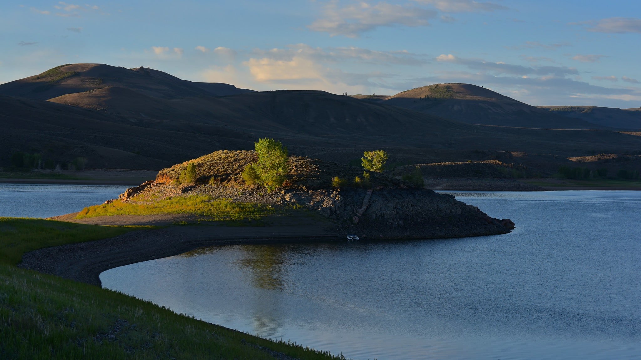 Dusk settles over Blue Mesa Reservoir. Blue water and green rolling hills with a small pennisula jutting out into the lake