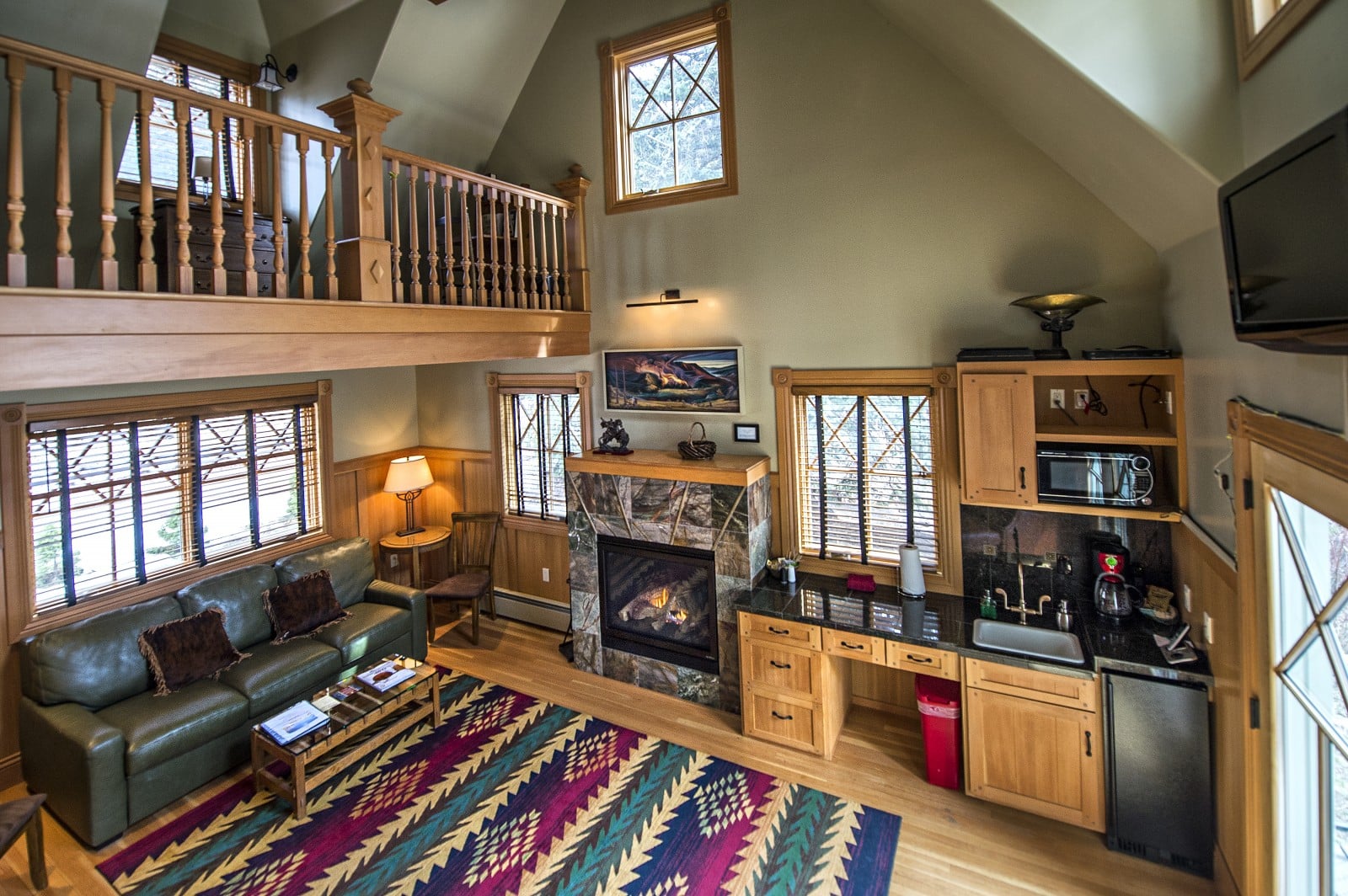 Two story room at the Redstone Inn. Large printed rug on hardwood floors with a kitchenette and fireplace in the sitting area. 