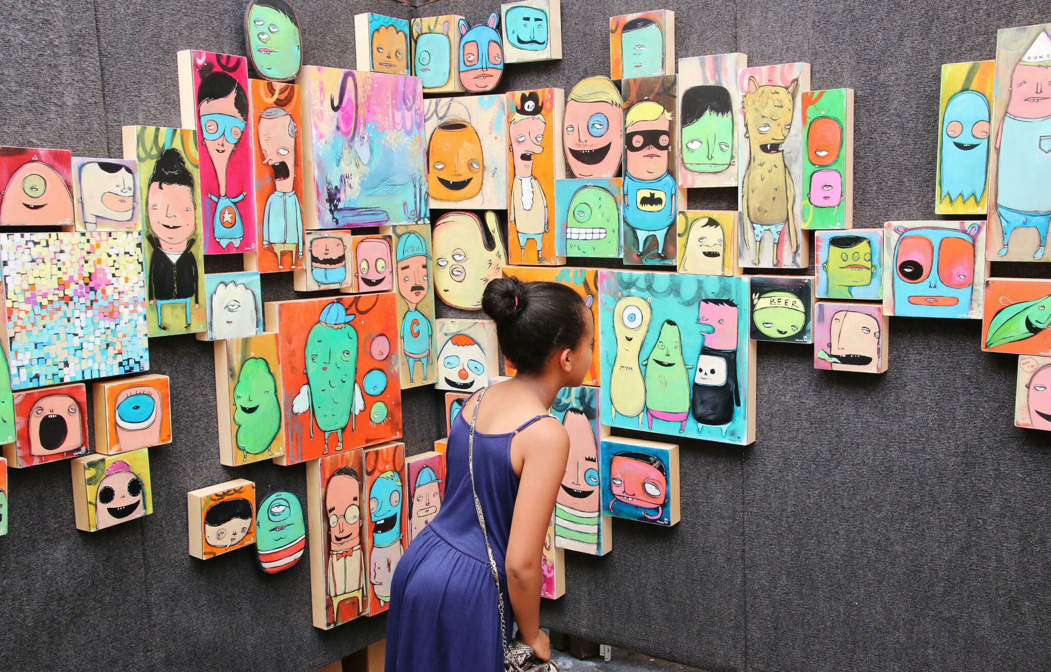 Visitor at the Cherry Creek Arts Festival in Denver looking at a display booth with a collage of colorful paintings of abstract faces by artist Chris Vance