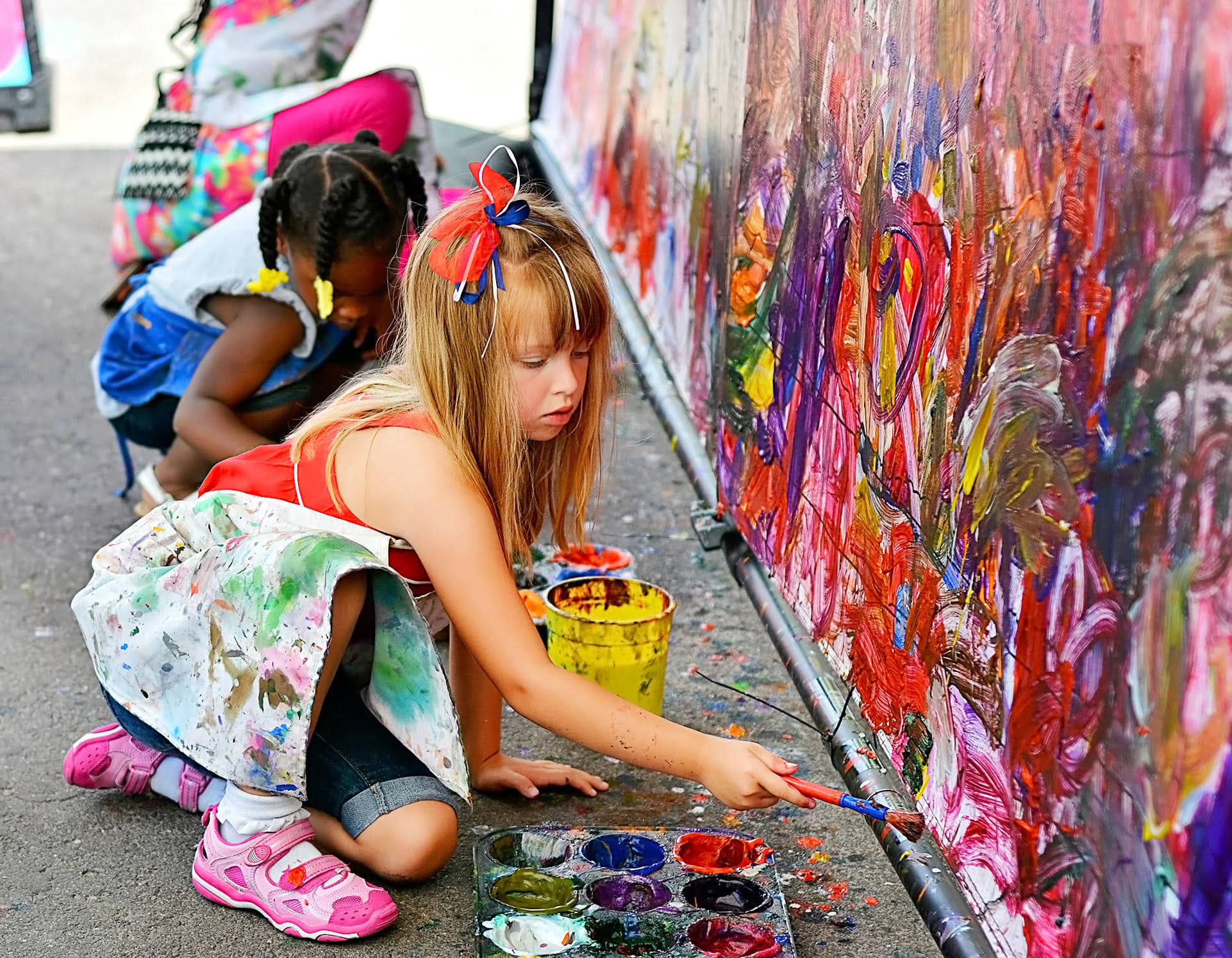 Young girl crouched down painting on abstract mural wall at the Cherry Creek Arts Festival