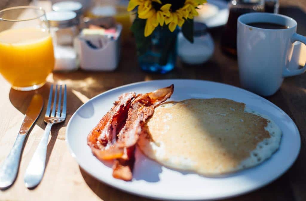 plate with slices of bacon and pancake, plus orange juice and coffee at Collective Vail Retreat