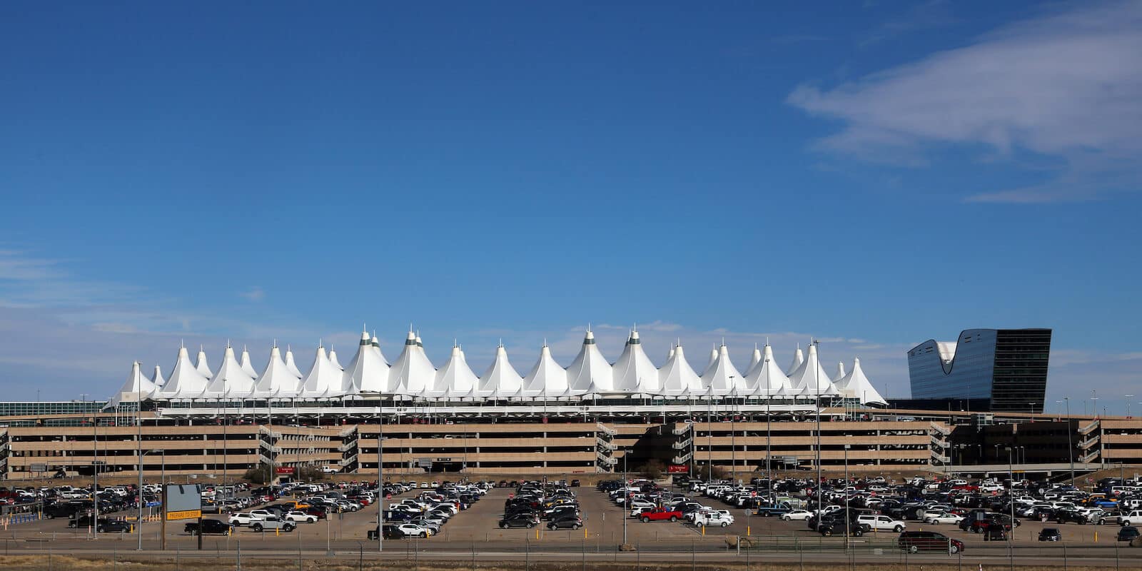 Exterior photo of the outside of Denver International Airport showing outside parking, covered parking garage, Jeppesen Terminal and Westin Airport Hotel