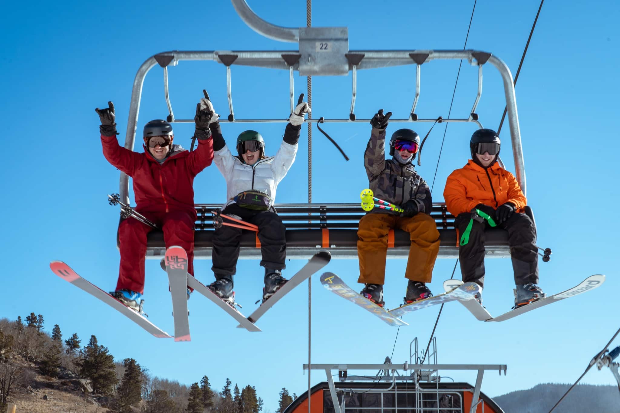 Four skiers on Eldora chairlift waving their arms and smiling at the camera.