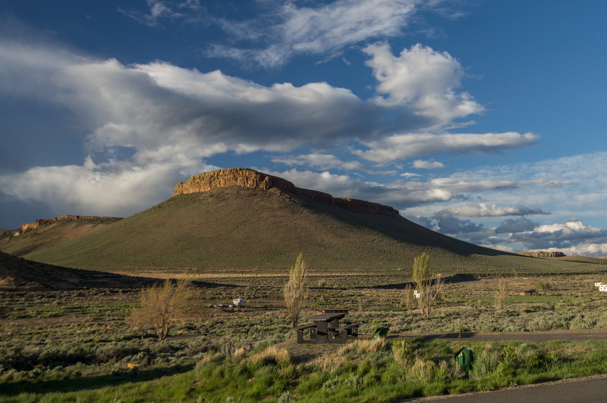 View of Curecanti National Recreation Area from Elk Creek campground. Large hill/mesa in the distance with grassy plains and blue, cloudy sky