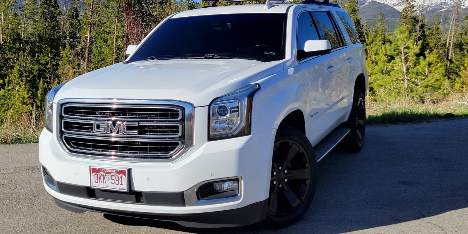 White GMC SUV parked in front of forest for Grand Mountain Rides