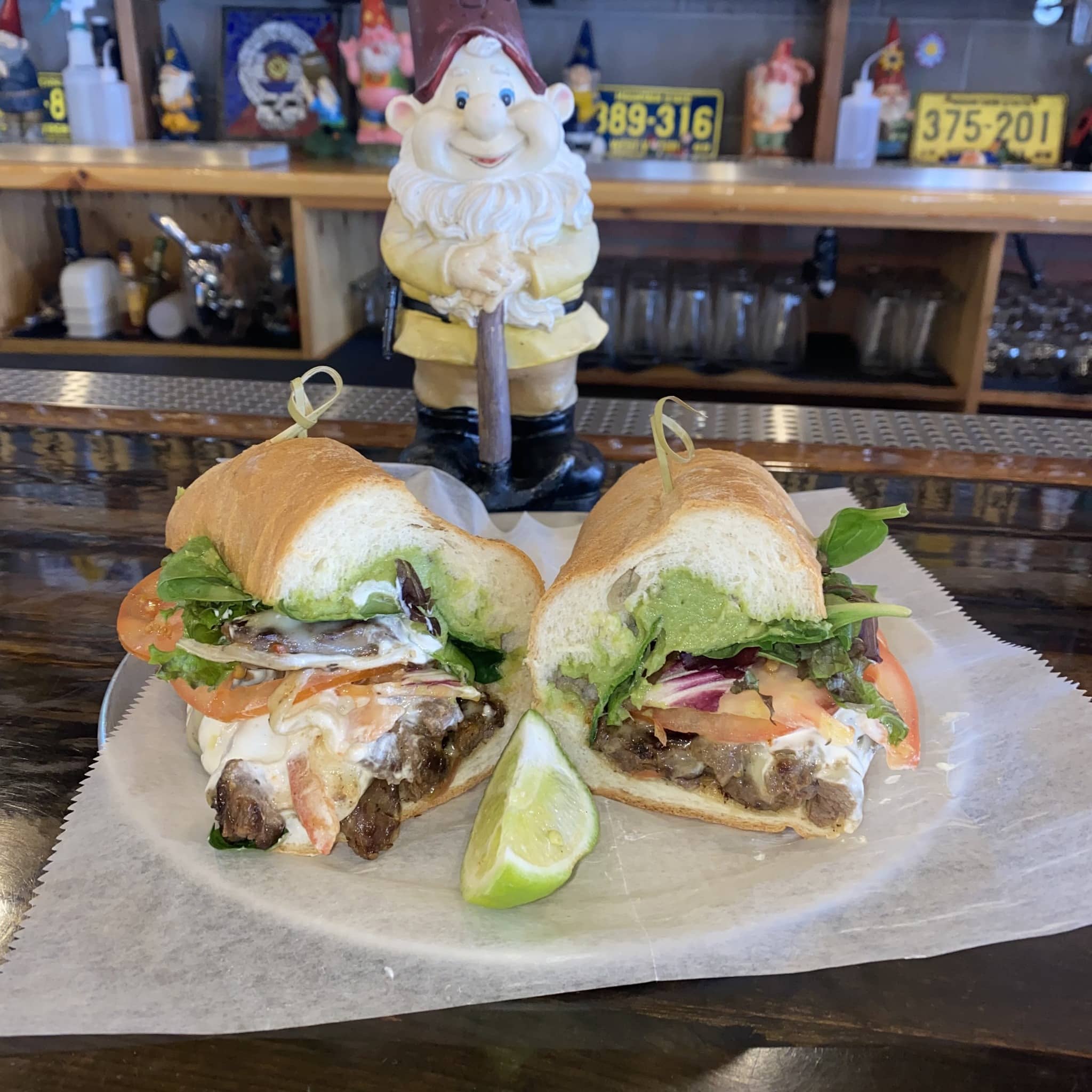 Small gnome statue standing behind a plate with carne asada sandwich at The Grateful Gnome Sandwich Shoppe & Brewery in Denver