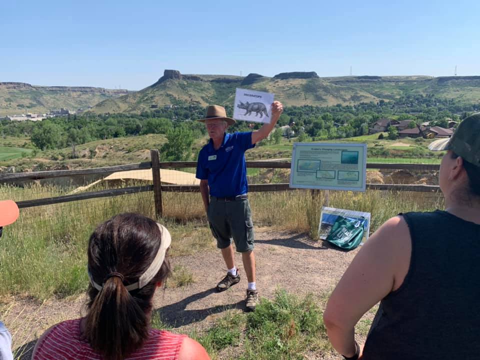 Tour guide at Dinosaur Ridge standing in front of small group of people holding up a picture of a Triceratops 