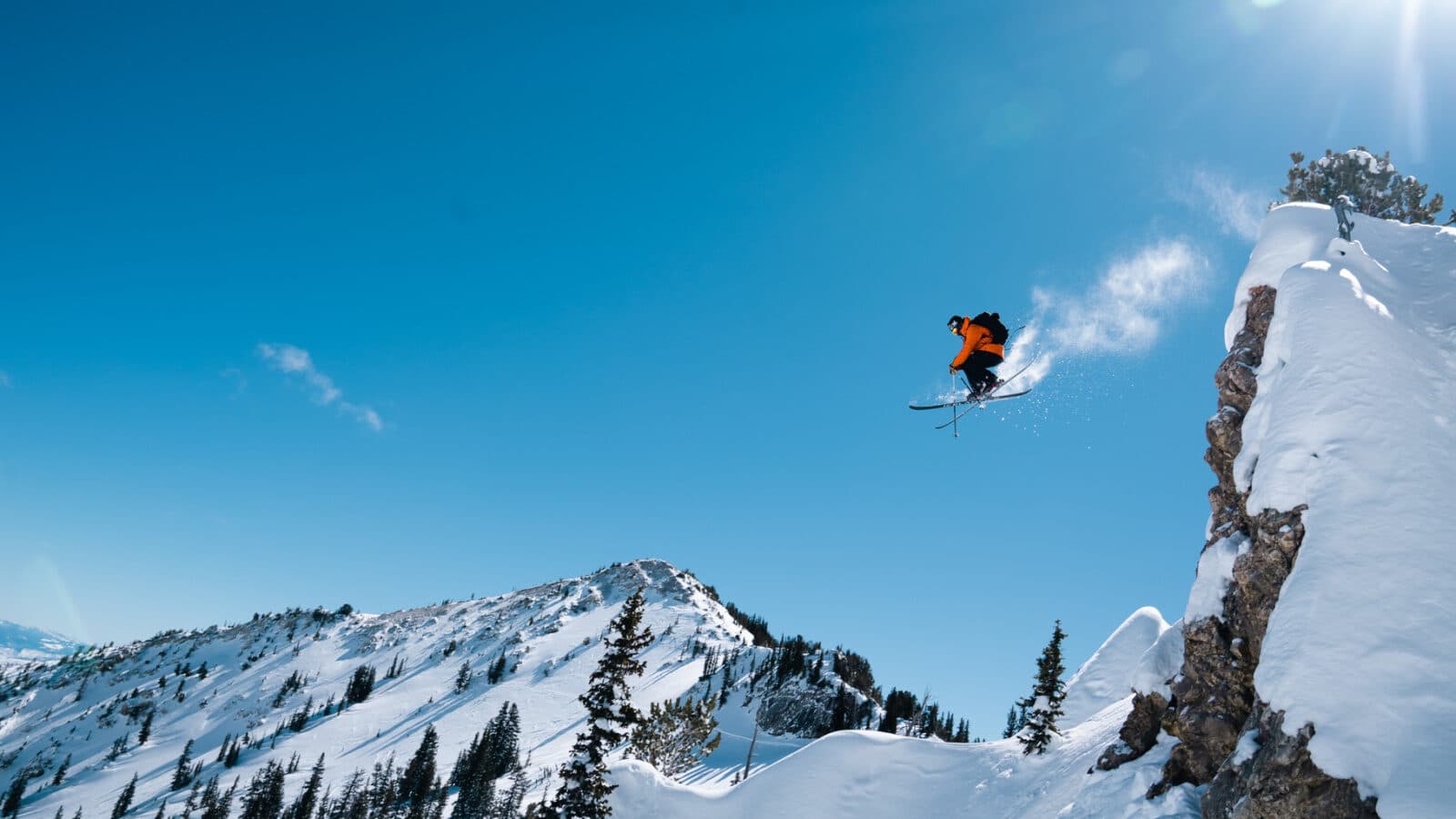 Skier in a red jacket on Icelantic Skis sending it off a huge jump on a bluebird skies day