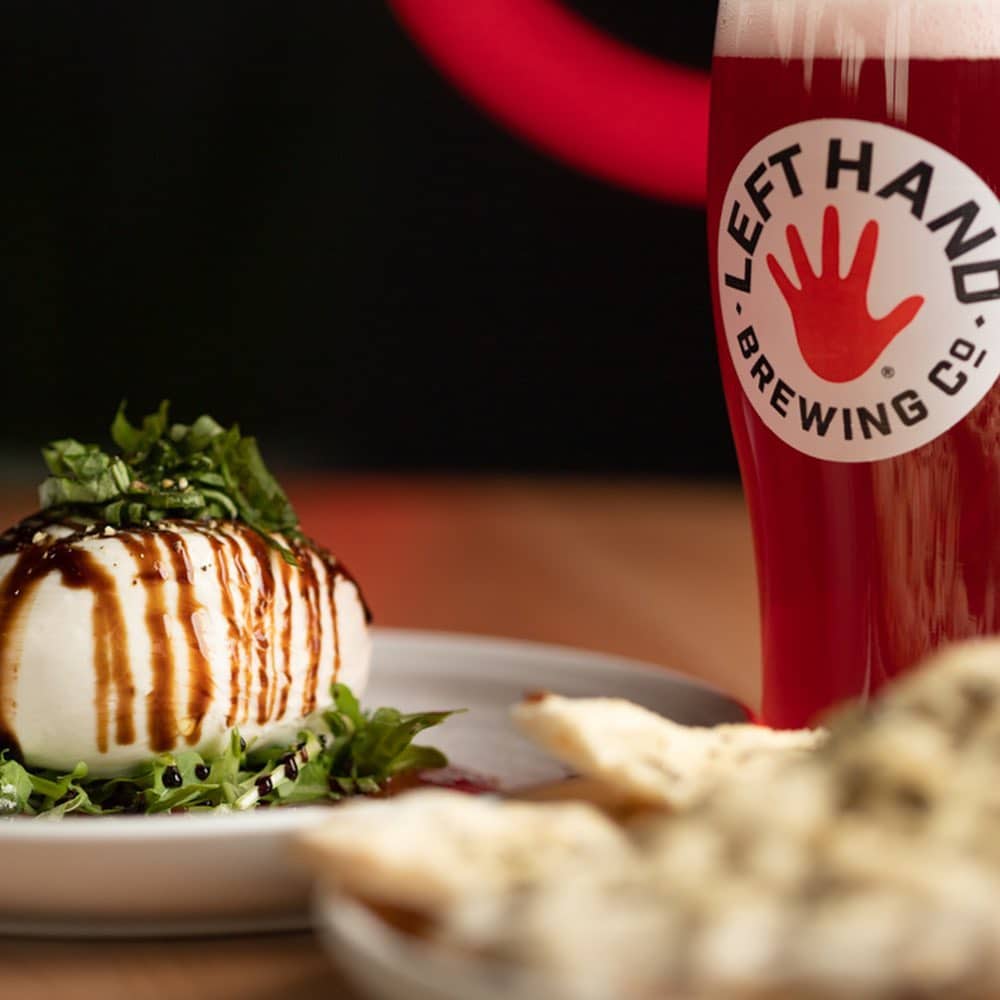 Mozzarella with balsamic drizzle and basil plated next to a glass of Left Hand Brewing Company beer