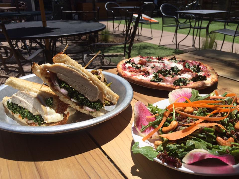 Outdoor table at Lowdown Brewery + Kitchen with 3 plates of food: 1 sandwich, 1 pizza, and 1 salad