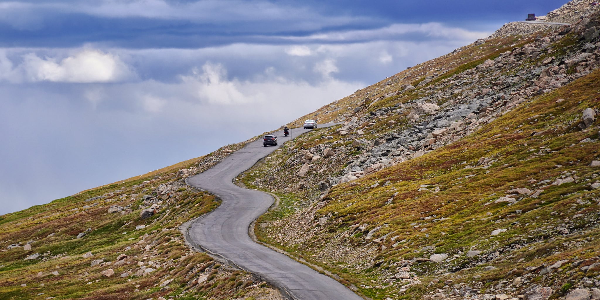 Car heading up Mt. Evans Byway with cloudy blue skies