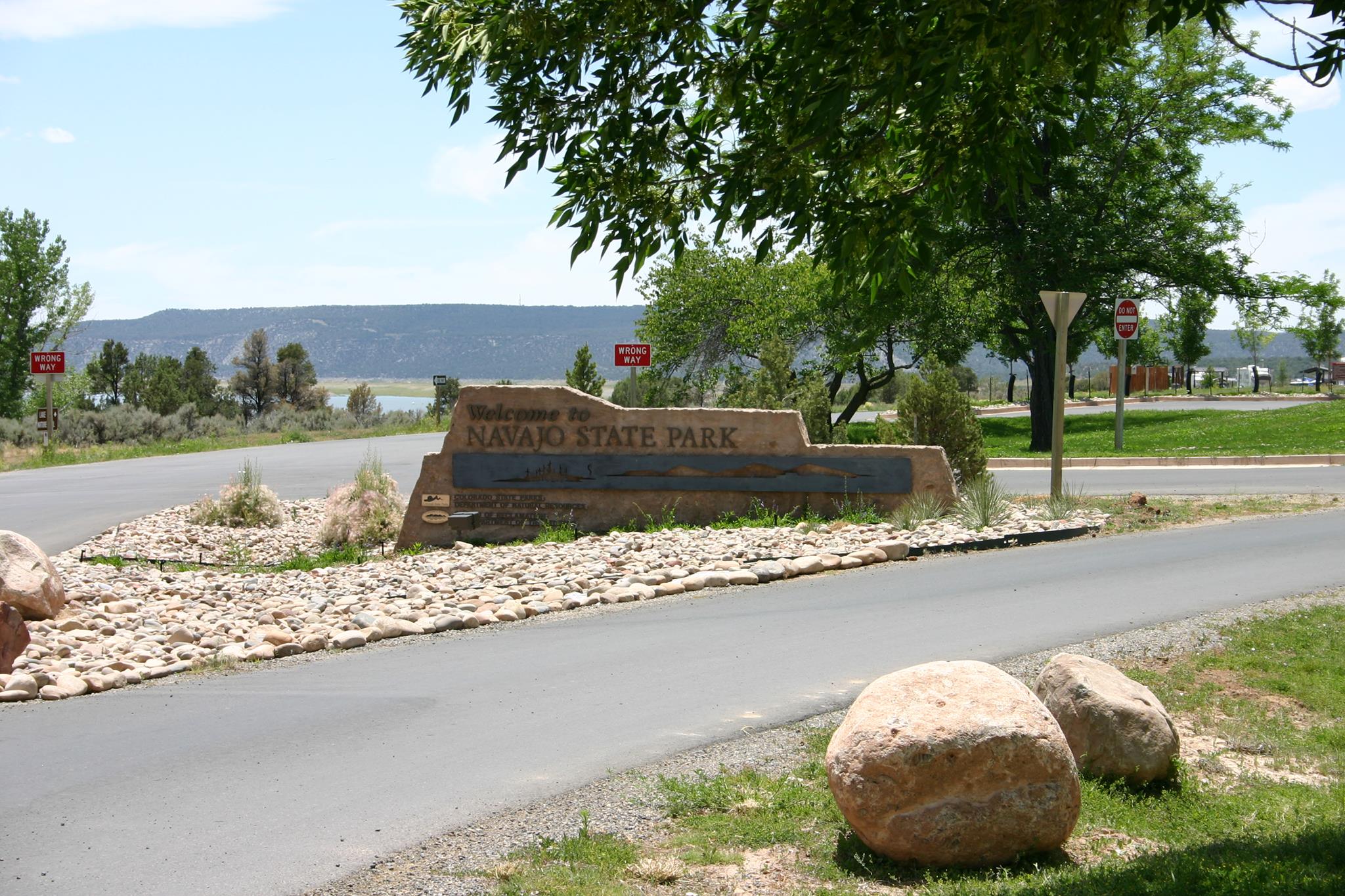 Rock entrance sign to Navajo State Park with asphalt road running in front of it to visitor center