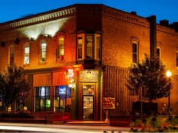 The Ore House Inn, a large brick building on a street corner at dusk, illuminated by uplighting.