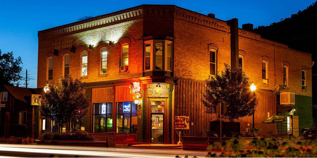 The Ore House Inn, a large brick building on a street corner at dusk, illuminated by uplighting.