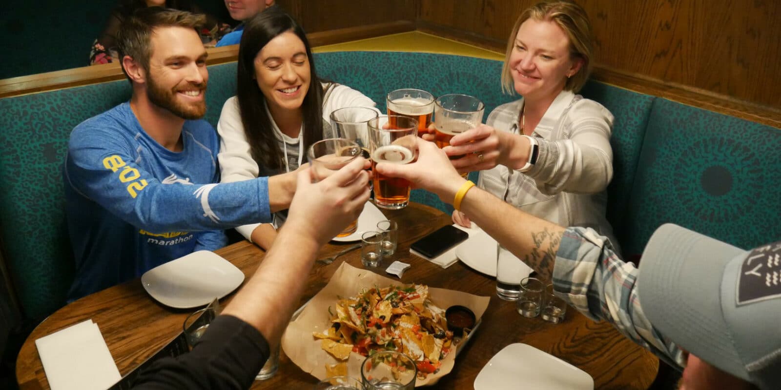 People sitting at a table in Oskar Blues Grill and Brew in Denver, toasting their beers over a plate of nachos