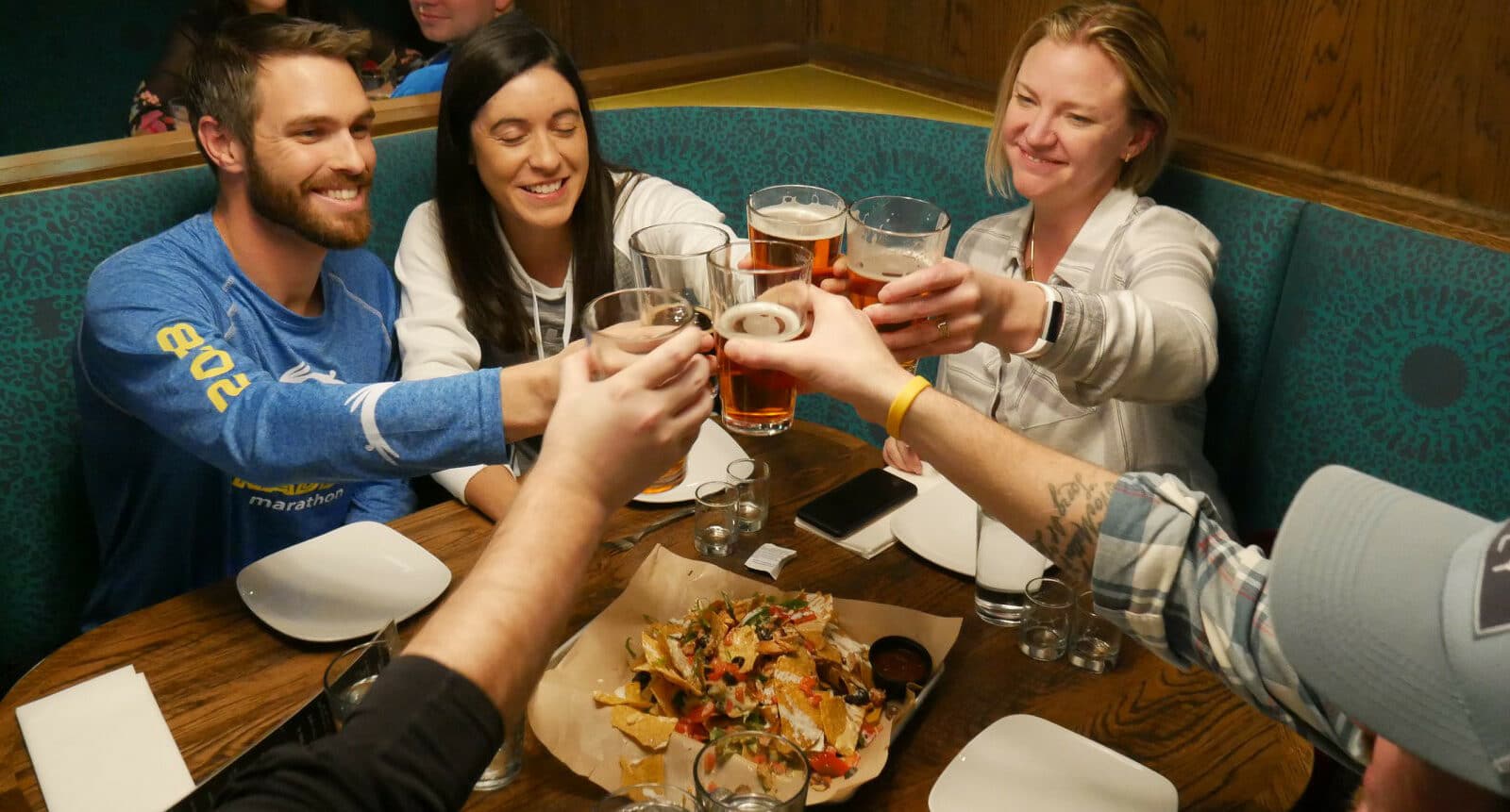 People sitting at a table in Oskar Blues Grill and Brew in Denver, toasting their beers over a plate of nachos