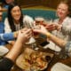 People sitting at a table in Oskar Blues Grill and Brew in Denver, toasting their beers over a plate of nachos