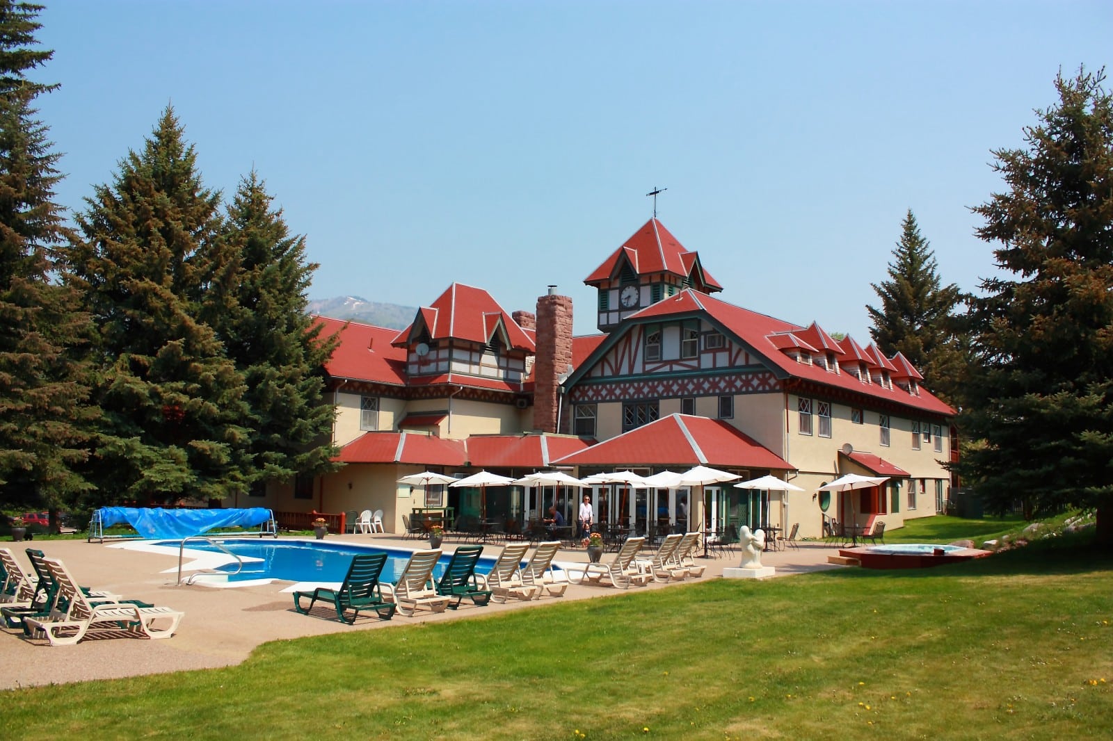 Back of the Redstone Inn property. White building with red roofing and a large concrete patio with a pool. Lawn chairs around the pool and a grassy area off to the side