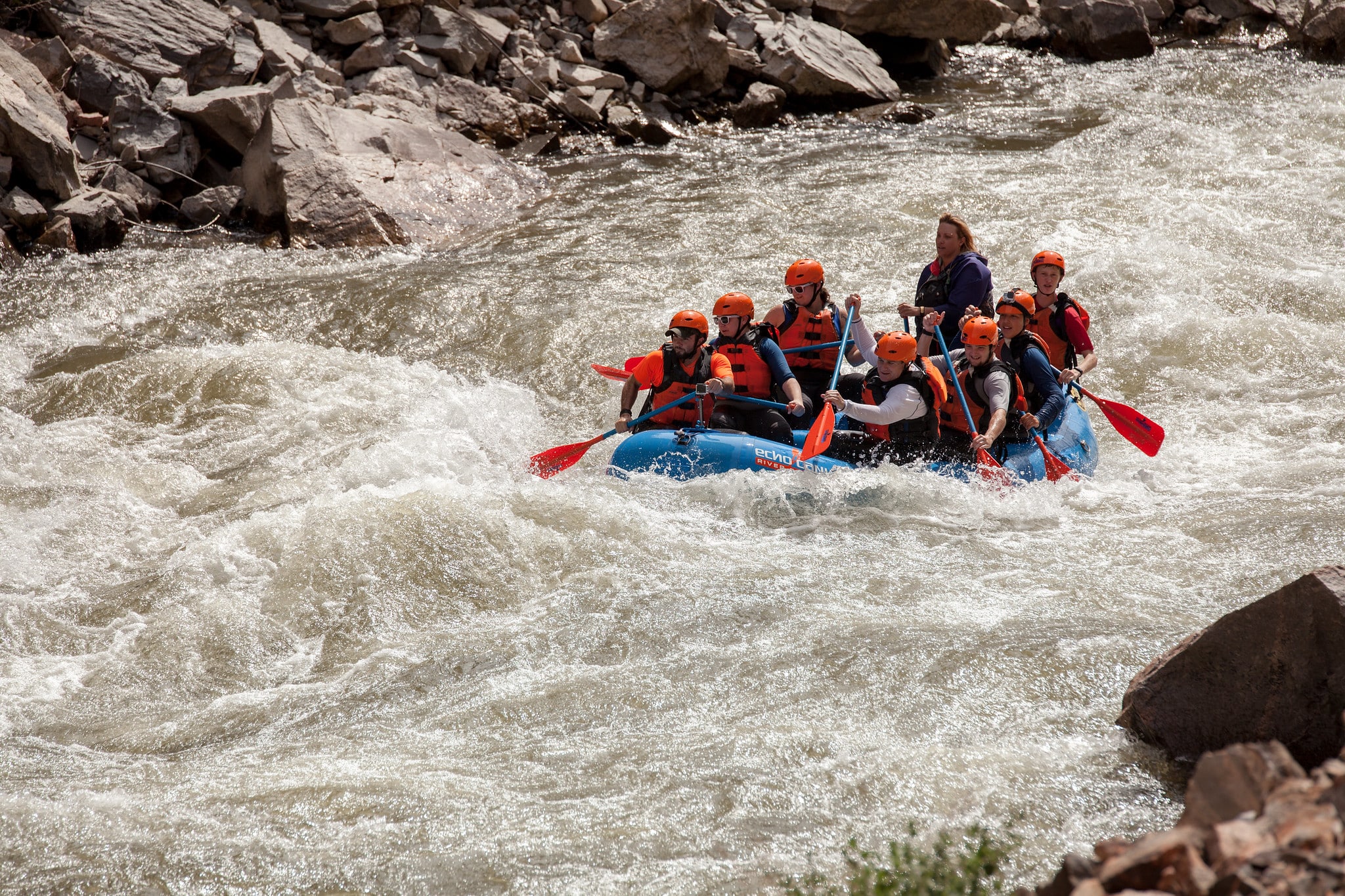 Group of people in a blue whitewater raft floating down a small set of rapids on the Arkansas River through the Royal Gorge