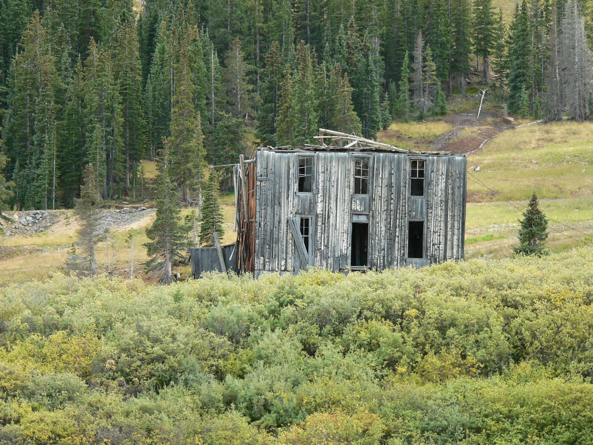 Abandoned mine in Summitville. Old wooden building that is grey, has 5 windows and a door and is surrounded by forestry