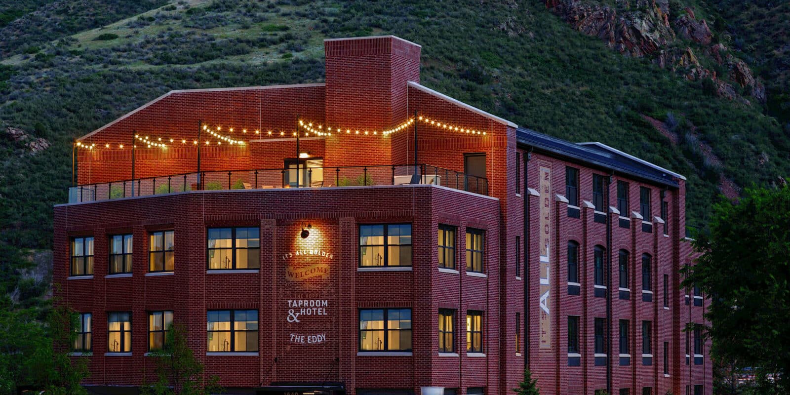 Exterior of The Eddy Taproom & Hotel. Brick 4 story building with a lighted outdoor patio on the top floor