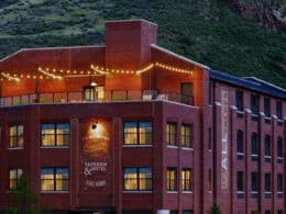 Exterior of The Eddy Taproom & Hotel. Brick 4 story building with a lighted outdoor patio on the top floor