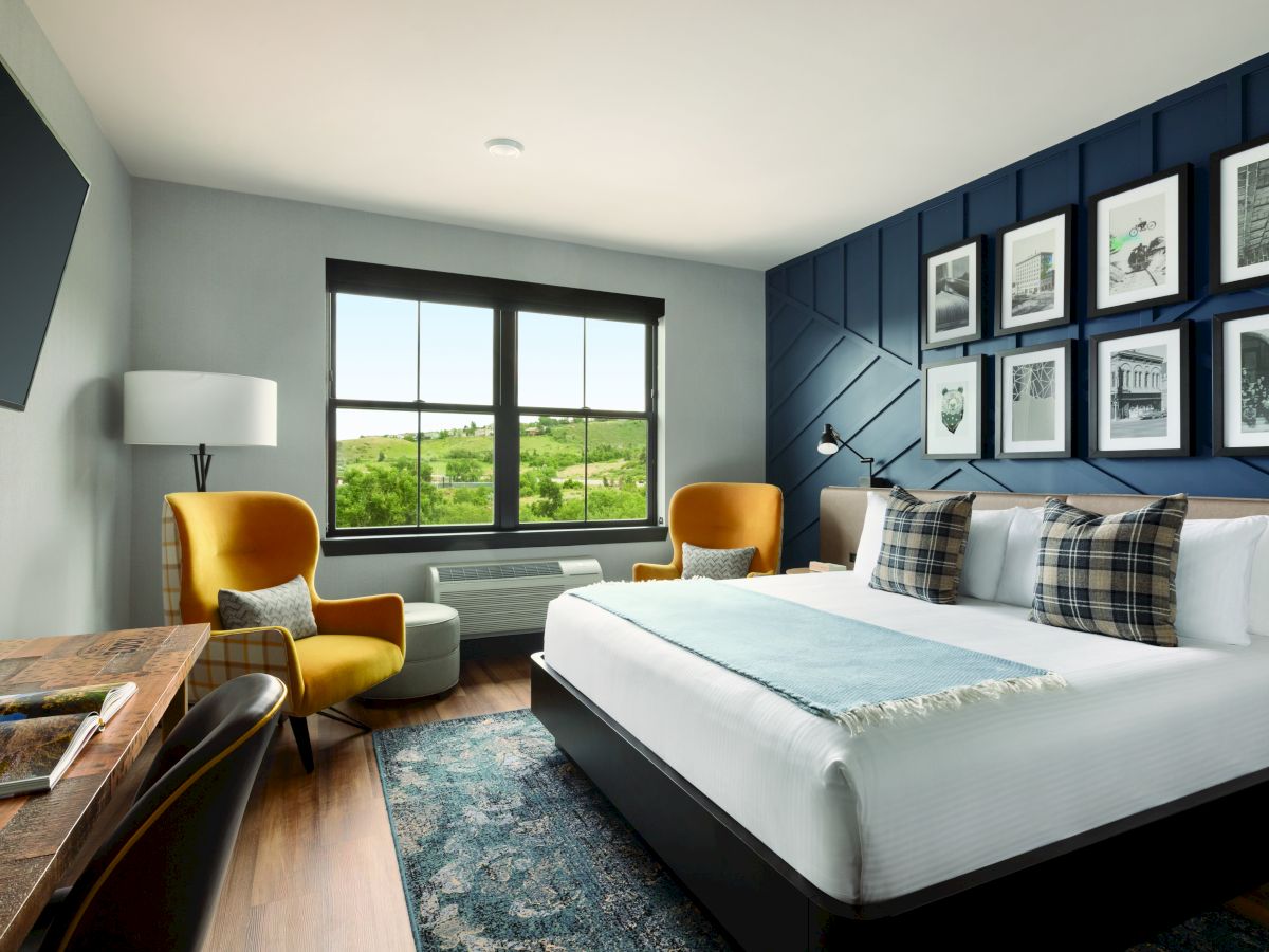 Hotel room with at the Eddy Taproom & Hotel. One king bed with white linens. Navy blue accent wall with black and white picture frames, wooden dresser and two yellow sitting chairs