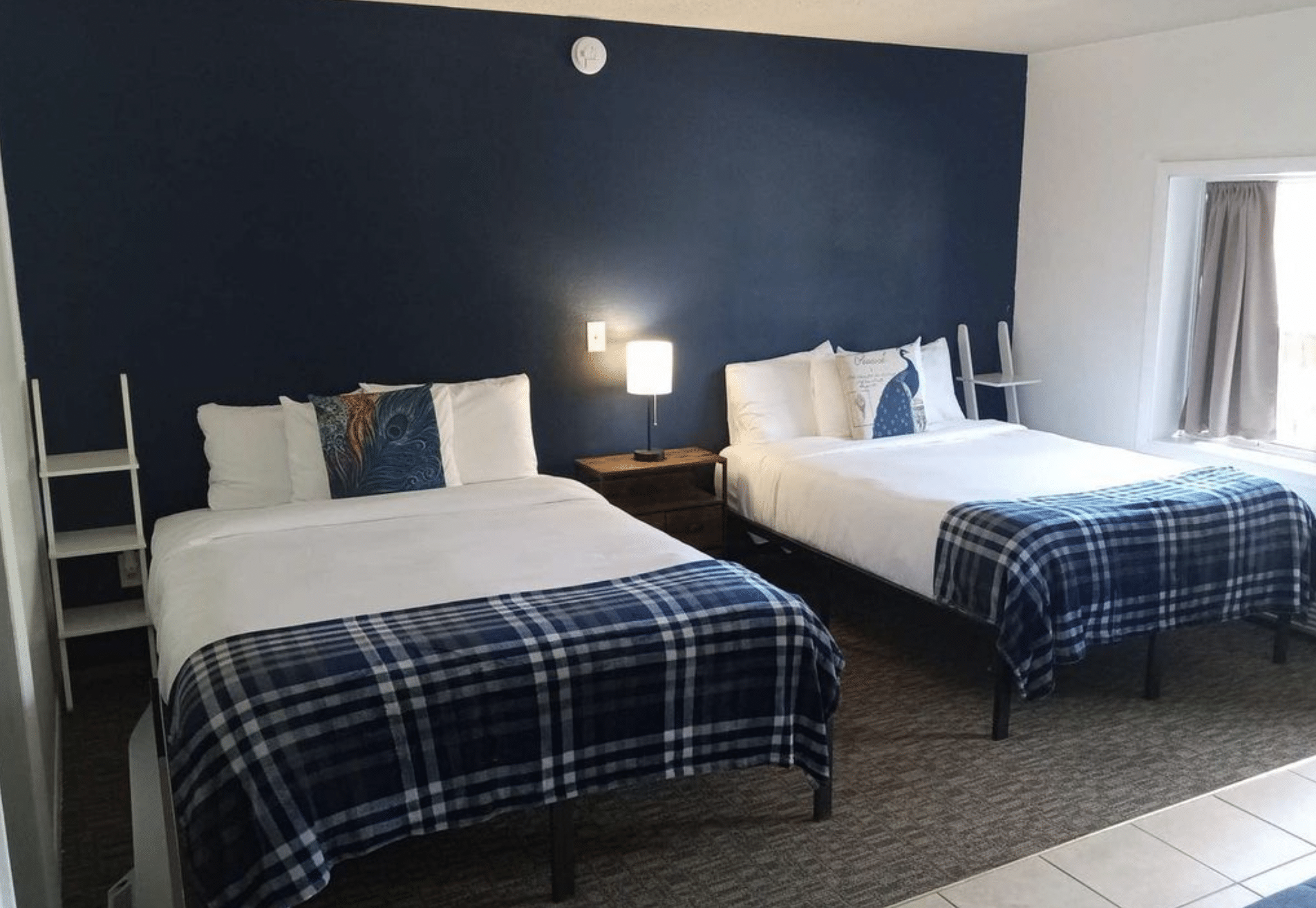 Guest room at The Alpine Motel in Collbran with two queen beds and a small nightstand in between. Navy blue accent wall behind the beds and white and blue linens on each bed