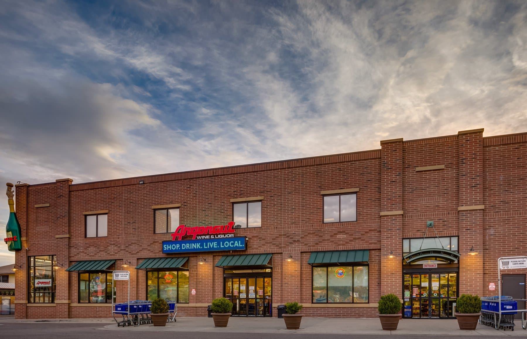 Storefront of Argonaut Wine & Liquor store in Denver. Two story brick building with red lettering spelling Argonaut and the beginnings of a sunset behind the building.