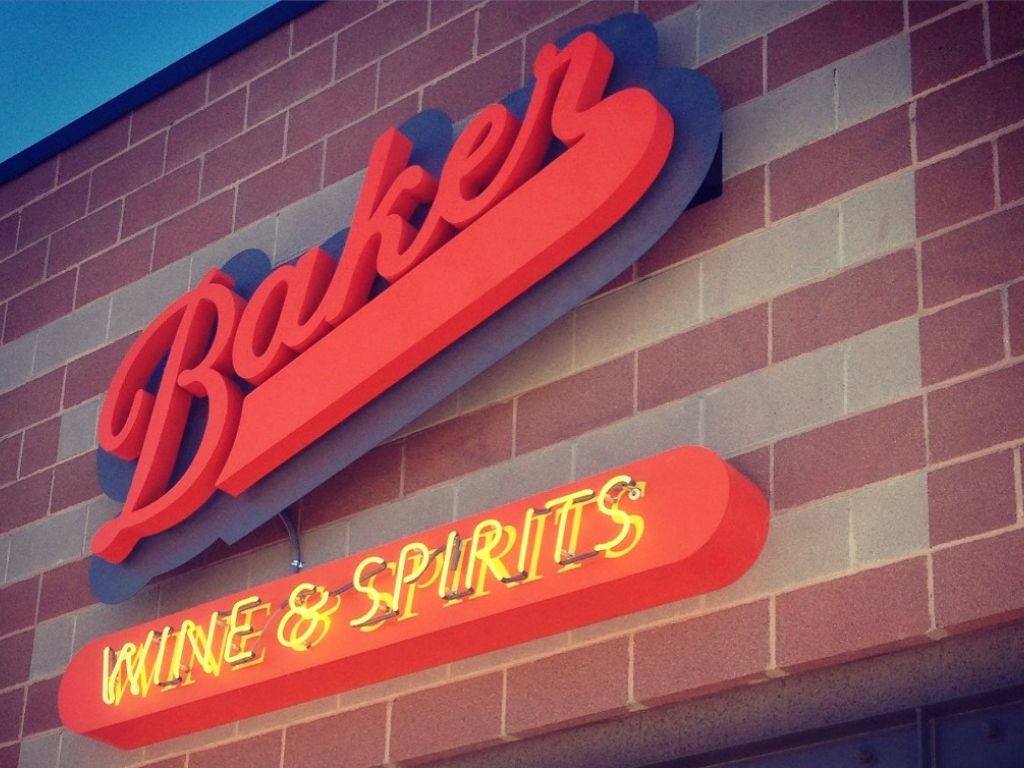 Store sign for Baker Wine in Spirits in red cursive font with yellow neon lettering