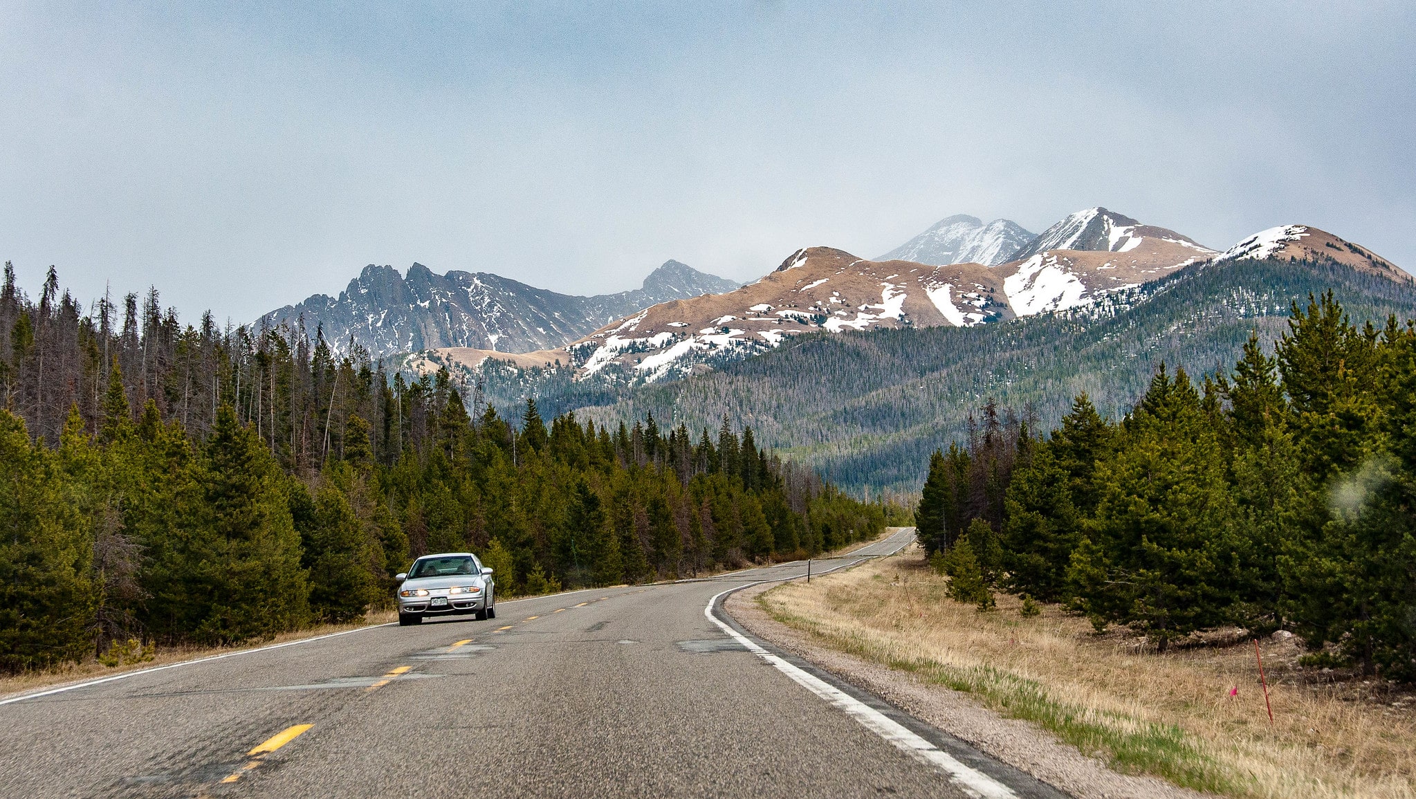 Cache La Poudre-North Park Scenic Byway road with one car coming toward the photographer. Mountains with snowcaps in the background